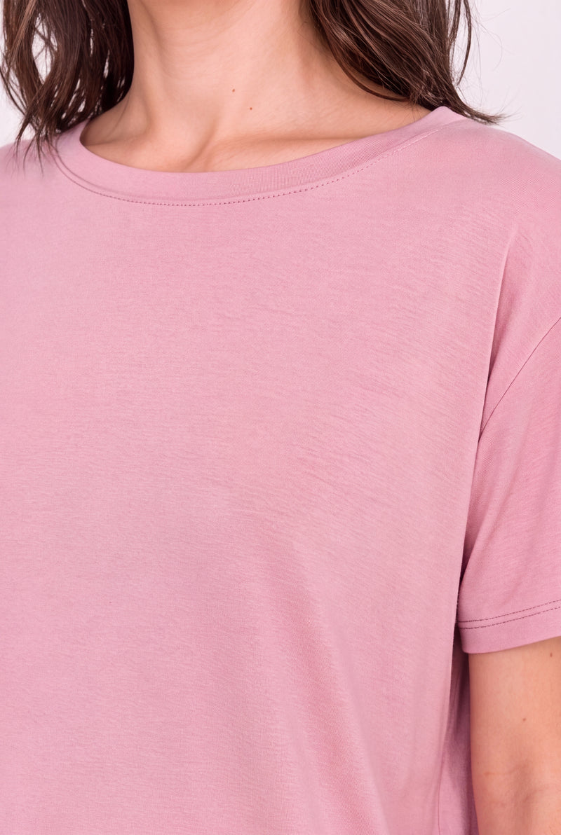 A close-up of a person wearing a soft dusty pink short-sleeve crewneck t-shirt, showing the fabric texture and neckline.