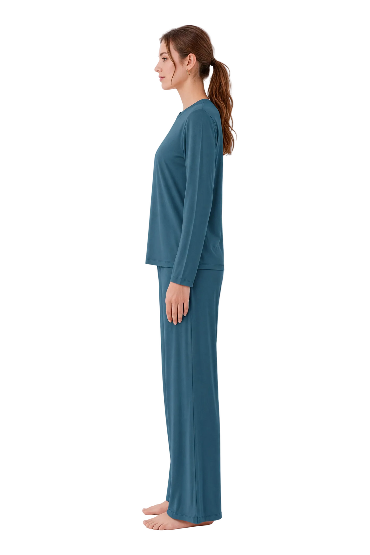 A woman stands in profile wearing a two-piece long-sleeve pajama set in a muted teal-blue color against a plain white studio background.
