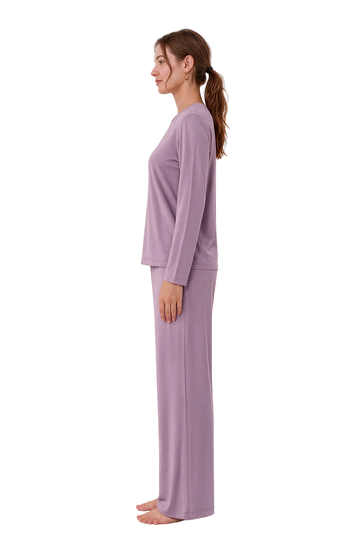 A woman in profile wearing a matching two-piece pajama set in a dusty lavender-purple color, standing barefoot against a plain white studio background.