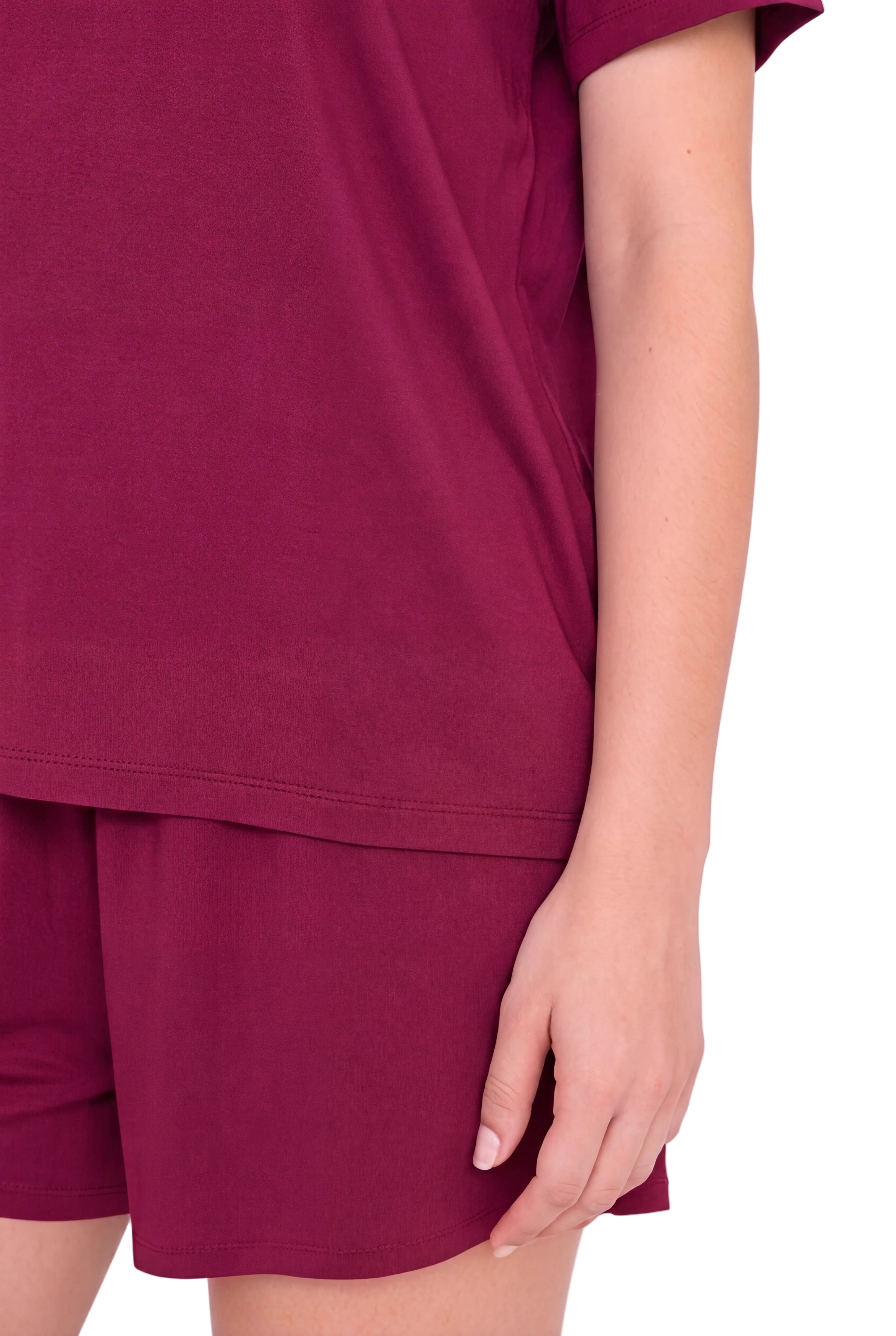 A close-up of a person wearing a matching burgundy short-sleeve top and shorts set, showing the side profile and hand against a plain light background.