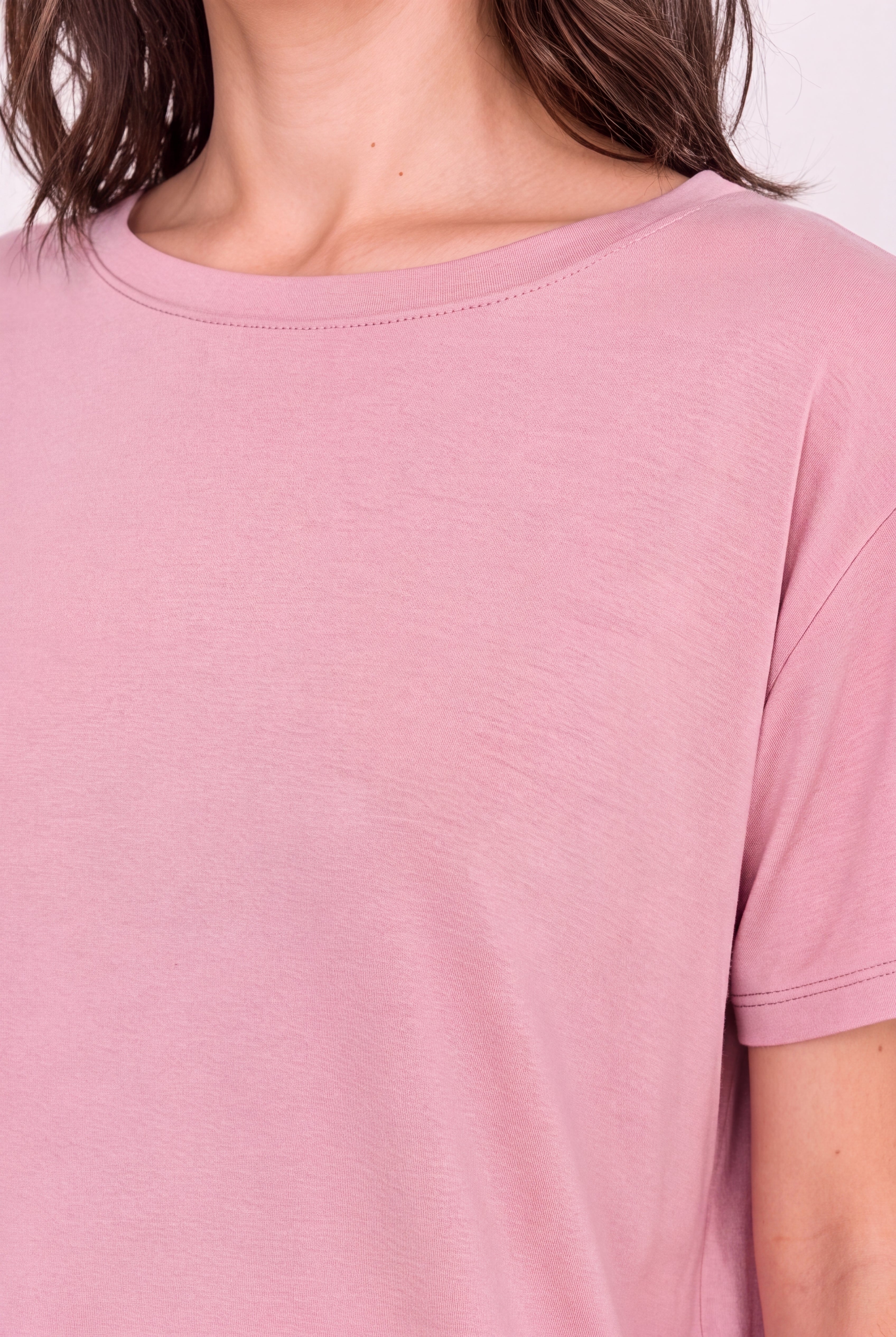 A close-up of a person wearing a soft dusty pink short-sleeve crewneck t-shirt, showing the fabric texture and neckline.