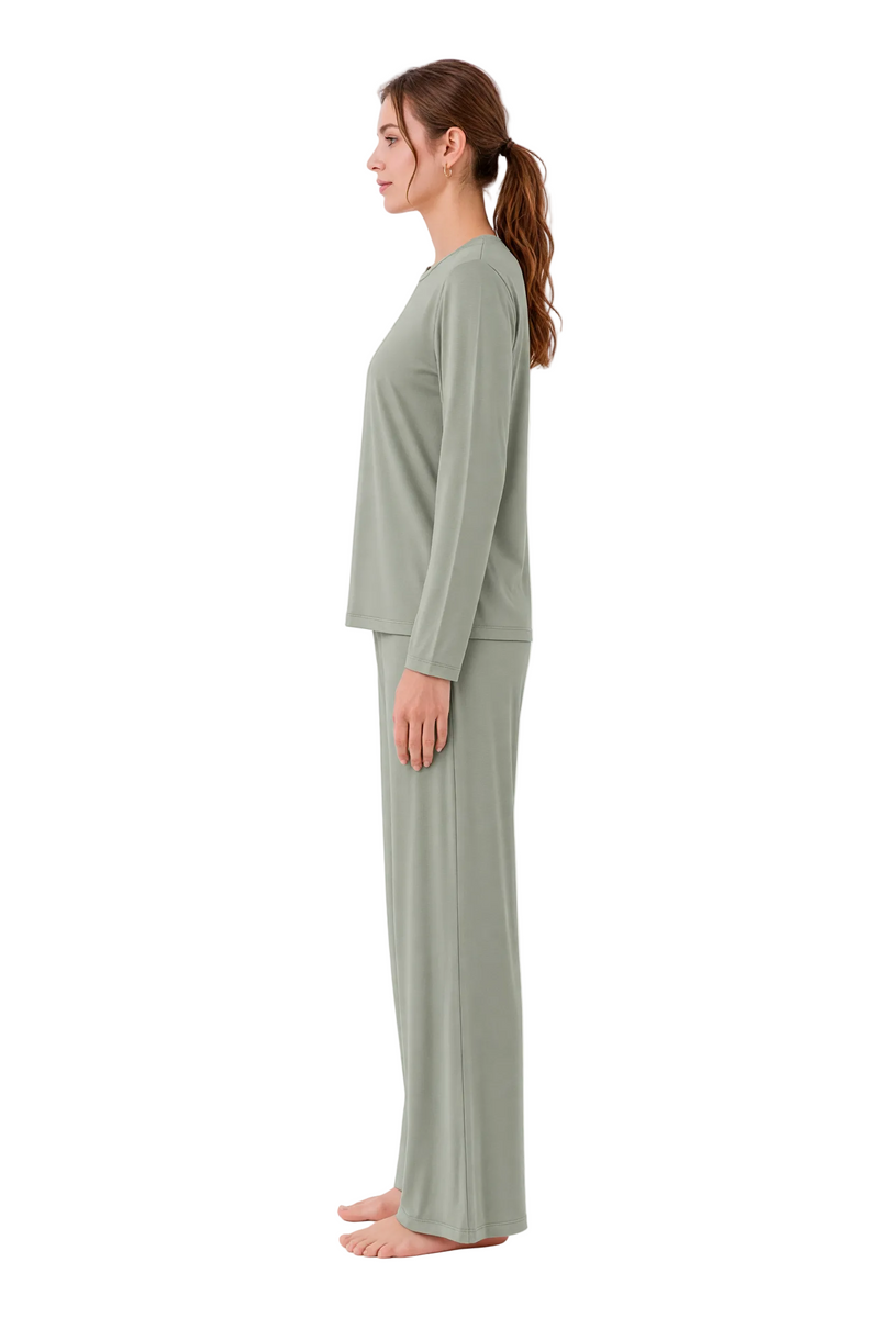 A woman stands in profile wearing a matching two-piece lounge set consisting of a long-sleeve top and wide-leg pants in a muted sage green color, set against a plain white studio background.